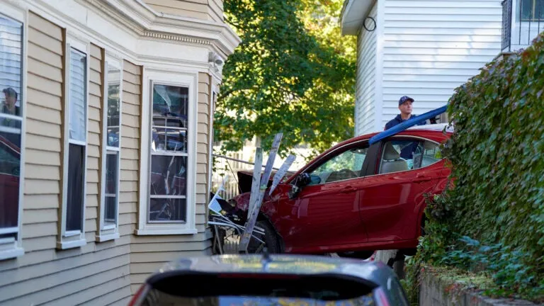 Car left suspended between house and fence after Jamaica Plain crash