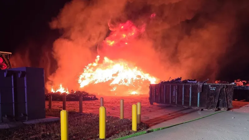 Flames from large metal scrapyard fire light up early morning sky, tower over Highway 90
